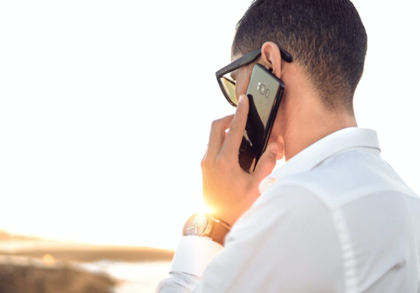 man holding smartphone standing in front of calm body of water